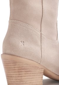 Bottine en daim beige avec talon en bois empilé et petit logo embossé près de la couture du talon.