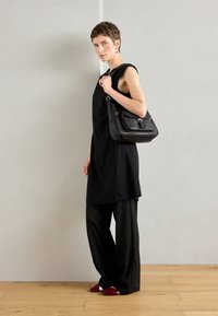Black sleeveless dress paired with loose black trousers, and red pointed-toe shoes. A black leather shoulder bag completes the look.