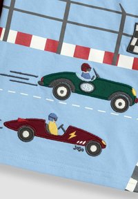 Tela azul claro con coches de carreras bordados: uno verde con un piloto azul y un coche rojo con un piloto amarillo, sobre un fondo simple.