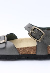 Sandale en cuir gris avec deux sangles ajustables, boucles en bronze, semelle intermédiaire en liège et semelle extérieure en caoutchouc noir texturé.