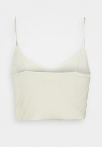 Top court côtelé ivoire clair avec fines bretelles spaghetti ajustables et décolleté en V. Tissu doux et extensible avec une coupe ajustée.