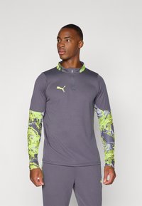 Gray long-sleeve shirt with a quarter zip, featuring vibrant green and purple patterned sleeves. Iconic logo on the chest. Athletic fit.