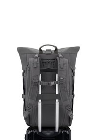 Mochila gris con un diseño de parte superior enrollable, correas acolchadas y herrajes metálicos. Cuenta con múltiples bolsillos y un panel de malla para ventilación.