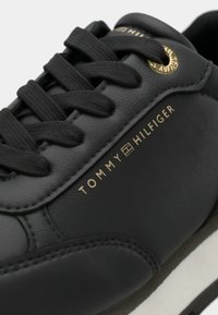 Svart sneakers med skinnoverdel, rund tå og tekstillisser. Har detaljering med gulllogo og teksturerte sidepaneler. Hvit gummisåle.