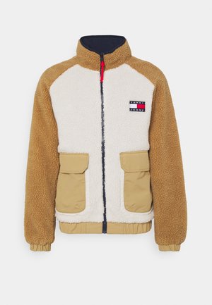 Veste en polaire avec manches beige, corps crème, deux poches avant, fermeture éclair marine et logo Tommy Jeans sur la poitrine.