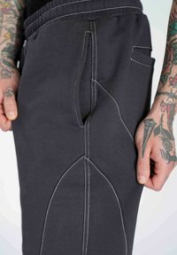 Sivé bavlnené tepláky s bielymi švami, s zakrivenými bočnými švami a vreckami, zobrazené od pásu po koleno.