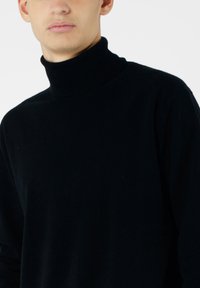 Czarny sweter z golfem wykonany z miękkiego materiału, z wysokim kołnierzem, luźnym krojem i długimi rękawami z minimalnymi detalami.