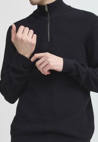 Dunkelblaues geripptes Strickpullover mit hohem Kragen und Frontreißverschluss. Verfügt über lange Ärmel mit engen Bündchen und strukturierter Stoff.