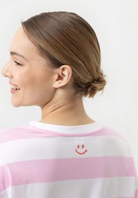 Gestreept T-shirt in roze en witte katoen, met een klein rood glimlachend gezichtje op de achterkant bij de halslijn. Korte mouwen en een ronde hals. 