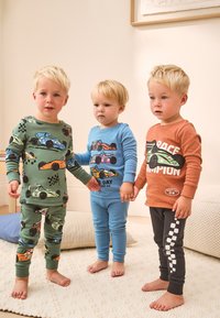 Trois tout-petits portant des pyjamas colorés avec des motifs de voitures. Vert avec plusieurs motifs, bleu avec une grande impression, et orange avec du texte.