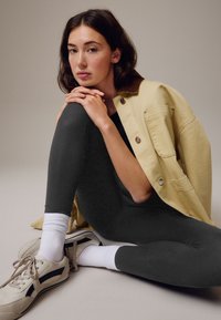 Leggings gris, veste crème avec col marron, chaussettes blanches et baskets avec une bande noire. Textures lisses, tenue décontractée.