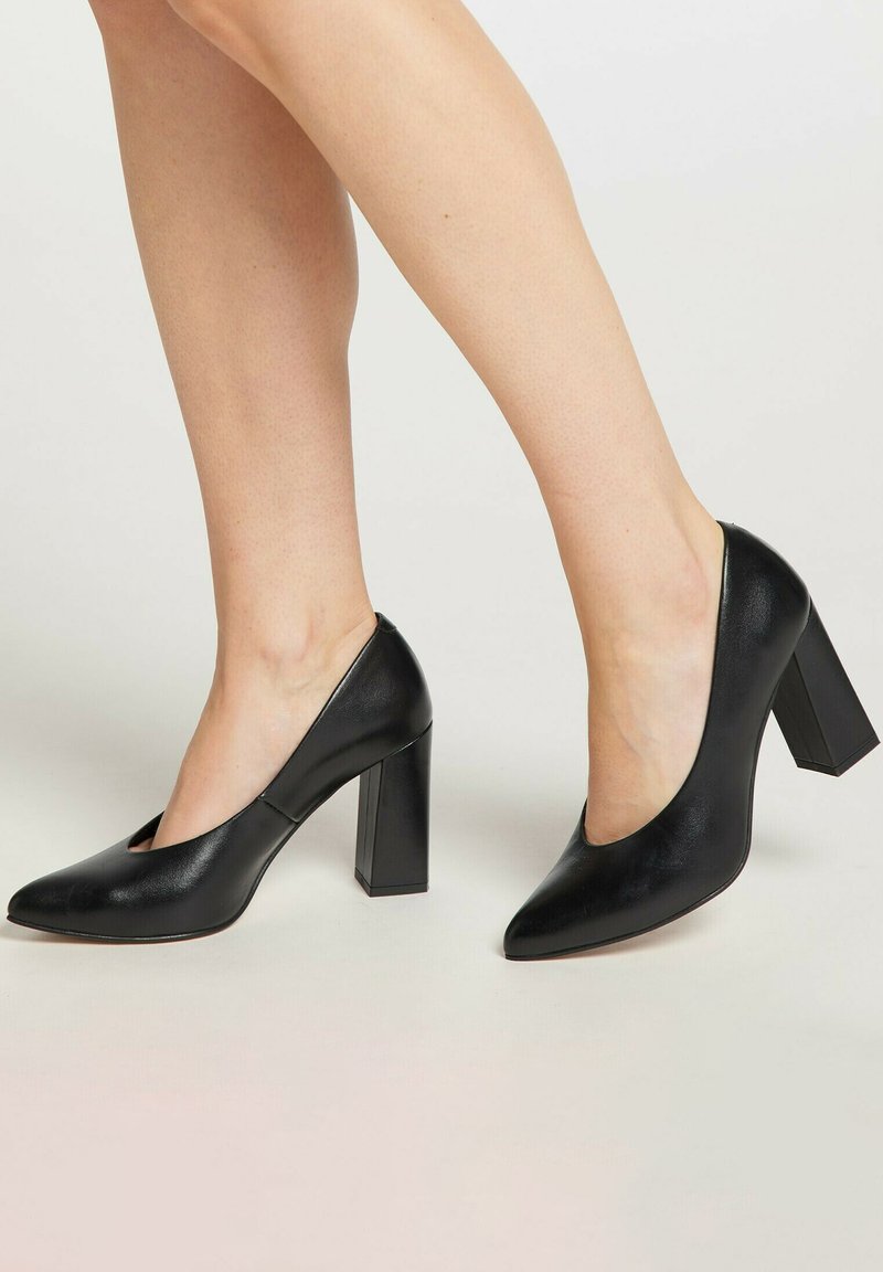 Schwarze Leder-Pumps mit hohen Absätzen, quadratischem Blockabsatz, spitzem Zehenbereich und seitlichen Ausschnitten. Glatte Textur mit glänzendem Finish.