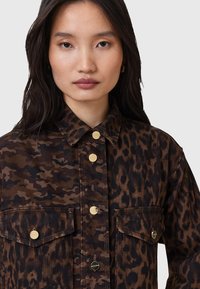 Camicia di jeans con stampa leopardata in tonalità di marrone e nero, con bottoni dorati, colletto e due tasche frontali. Tessuto con finitura testurizzata.