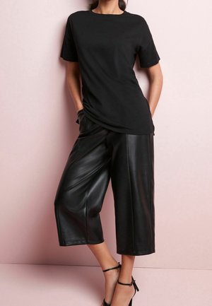 Czarna koszulka z krótkim rękawem w połączeniu z czarnymi skórzanymi spodniami culottes o wysokim stanie. Gładka tekstura, luźny krój i minimalistyczny design.