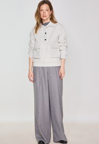 Sweatshirt gris clair avec un col, trois boutons et deux poches avant, associé à un pantalon large gris et des chaussures noires.