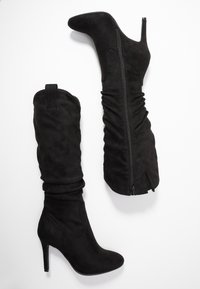 Dos pares de botas de ante negro: una hasta el muslo con cremallera y fruncidos, y la otra hasta el tobillo con un diseño elegante y un tacón alto.