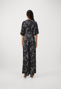Black jumpsuit featuring an all-over white circle and signature pattern, with short puff sleeves and a flowing silhouette down to the ankles.
