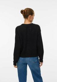 Black knitted sweater with a ribbed texture, round neck, and drop shoulders. Paired with light blue high-waisted jeans.