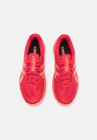 Chaussures de sport rouges avec une tige en maille respirante, des détails texturés et une semelle rembourrée. Présente des rayures blanches contrastantes et un logo.