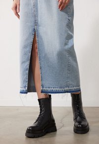 Svart lær snørebåndstøvler med en tykk plattformsåle, kombinert med en lys blå denimskjørt med en frontsplitt og frayed kant.