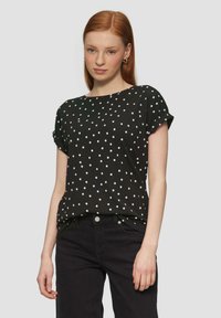 Zwarte kortekorte mouwen shirt met witte stippen, ronde halslijn, zachte stof, comfortabele pasvorm, gedragen met zwarte broek. Geen zichtbare logo's of versieringen.
