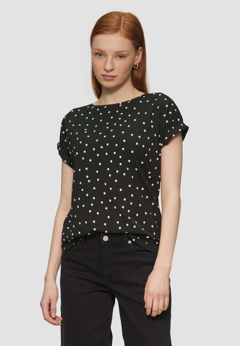 Zwarte kortekorte mouwen shirt met witte stippen, ronde halslijn, zachte stof, comfortabele pasvorm, gedragen met zwarte broek. Geen zichtbare logo's of versieringen.