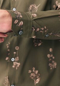 Vihreä, kukkakuosinen pitkähiha-paita, jossa on vaaleanbeigejä kukkia, nappisulkemiset ja teksturoitu kangas.
