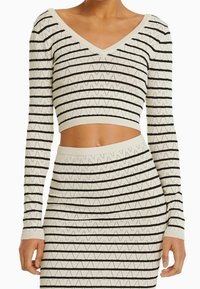 Virkat crop top och kjolset i krämfärg med svarta zigzag ränder och öppet stickat mönster, med långa ärmar och V-ringning.