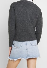 Grau gestrickter Pullover mit rundem Ausschnitt, gerippten Bündchen und Saum, kombiniert mit einem hellblauen Denim-Minirock mit fransigen Kanten.