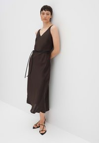 Abito in satin marrone con scollatura a V e spalline larghe, caratterizzato da una cintura nera in vita. Texture liscia e design lungo fino alla caviglia.