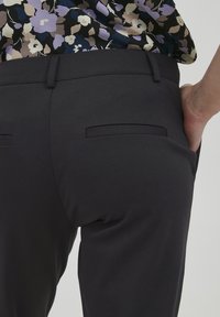 Mustad mustad püksid siledast kangast, tagumine taskud ja sobiv disain. Kantud mitmevärvilise lillemustriga särgiga.