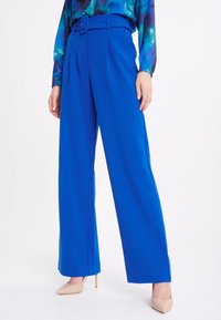 Pantalons larges bleu vif avec une taille haute et une ceinture assortie. Tissu lisse avec des plis pressés et une coupe ajustée.