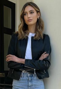 Black cropped leather jacket with silver zippers, paired with a white t-shirt and light blue high-waisted jeans. Smooth texture, minimal design.