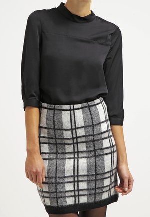 Femme portant un chemisier en satin noir à manches trois-quarts et une jupe en laine noire et blanche à carreaux taille haute.