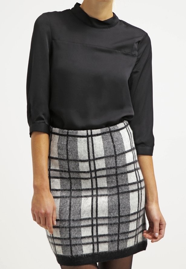 Femme portant un chemisier en satin noir à manches trois-quarts et une jupe en laine noire et blanche à carreaux taille haute.