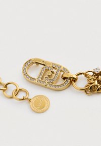 Náušnica so zlatým tónom a zapínaním s vkladanými čírymi rhinestones, spojená s okrúhlym zlatým reťazcom a malým značkovým okrúhlym príveskom.