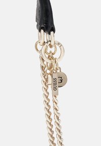 Cintura in pelle nera con hardware dorato, caratterizzata da anelli intrecciati, catene e un piccolo tag rettangolare con il nome del marchio "GUESS."