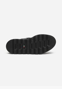 Suola di scarpa in gomma nera con profonde scanalature, motivi a scanalatura e un piccolo dettaglio della bandiera italiana vicino al centro.