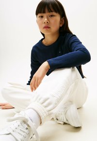 Marinblå stribet langærmet top, hvide trangt sweatpants med samlede manchetter og hvide sneakers. Simpelt design, ingen synlige mønstre eller logoer.