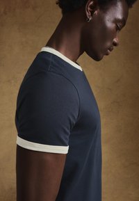 Tengerészkék póló fehér bordázott, környakú nyakkivágással és ujjszélekkel, testre szabott kialakítással és sima textúrával. Portré orientáció.