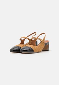 Tan woven slingback heels with black patent leather toe caps and a chunky heel. Features ankle strap and open sides for ventilation.