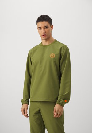 Oliven grønn langermet skjorte med elastisk mansjett, med et sirkulært oransje logo på brystet. Myk, matt stofffinish.