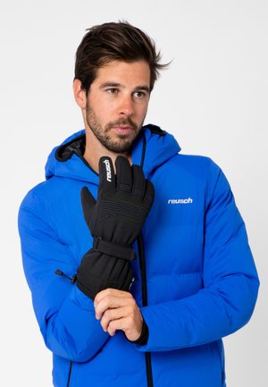 Schwarze isolierte Handschuhe mit einer strukturierten Oberfläche und einem verstellbaren Handgelenkband, getragen von einer Person in einer blauen Daunenjacke.