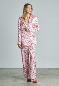 Completo floreale nei toni del rosa e del viola con giacca su misura e pantaloni a gamba larga, abbinato a scarpe rosa coordinate.