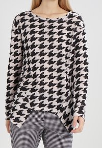 Pull à manches longues en tissu doux avec un motif pied-de-poule noir et crème, doté d'un col rond et d'une fente sur les côtés à l'ourlet.