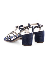 Denim High-Heelsandalen mit klobigem Blockabsatz, mehreren Riemen, goldenen Nietenakzenten und geschlossenem Absatz. Blauer Stoff mit hellen Nuancen.