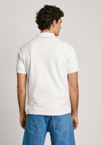 White short-sleeve polo shirt with blue and purple patterns, soft fabric, classic collar, and a straight hem, paired with blue denim shorts.