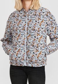 Květinová bomber bunda s světle modrým pozadím, smíchaným s oranžovými, bílými a růžovými květinami. Má přední zip a přiléhavé manžety.