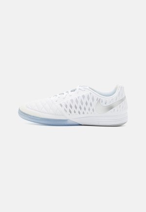 Biały halowy but do piłki nożnej Nike z siateczkowymi panelami bocznymi, pikowanym noskiem i półprzezroczystą podeszwą, widoczny od zewnętrznej strony.