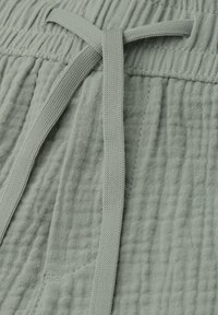 Tissu texturé gris clair avec un cordon plat noué au-dessus d'une poche avant et une couture à la taille élastique.